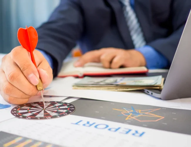 Businessman holding a darts aiming at the target center of dart board, Setting challenging business goals And ready to achieve the goal concept.